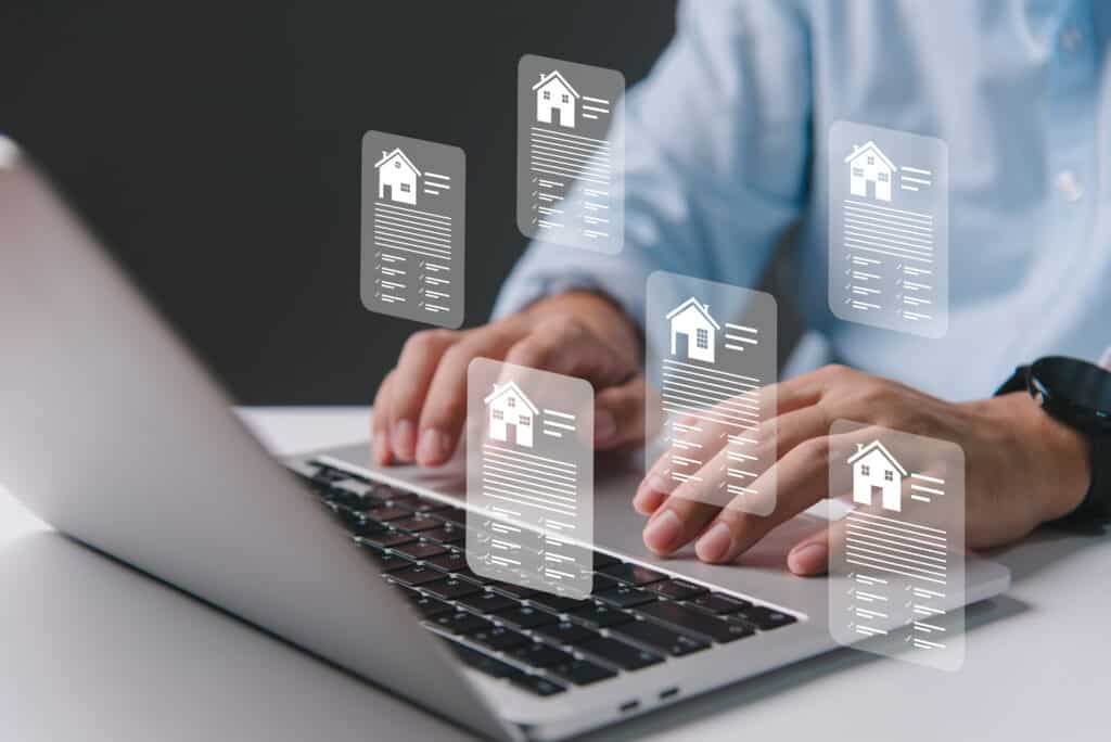 Mains tapant sur un ordinateur portable affichant des documents immobiliers numériques translucides avec des icônes de maisons et des listes de contrôle.