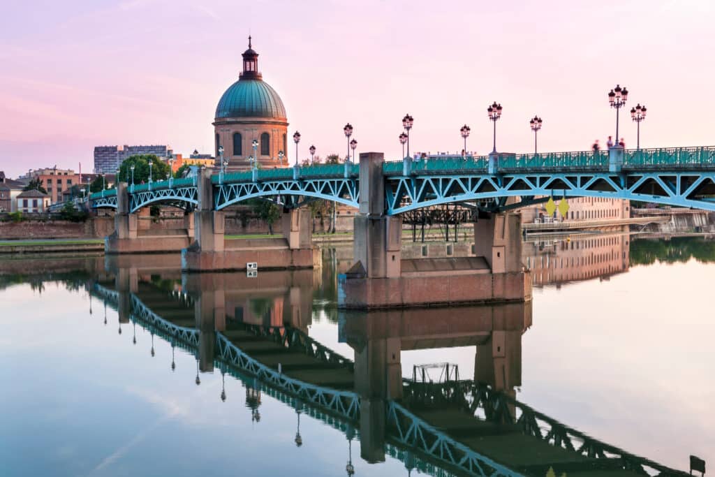 Toulouse: Pont Saint-Pierre & Dôme de La Grave au Crépuscule Pont Saint-Pierre et dôme de La Grave se reflètent dans la Garonne à Toulouse. Ciel rose crépusculaire, lampadaires et marqueur 'III'.